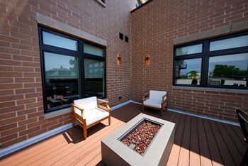 A patio with two chairs and a table with a fire pit in the middle.